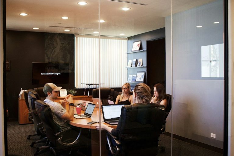 A diverse group of people enthusiastically gathered around a laptop, smiling and engaged.